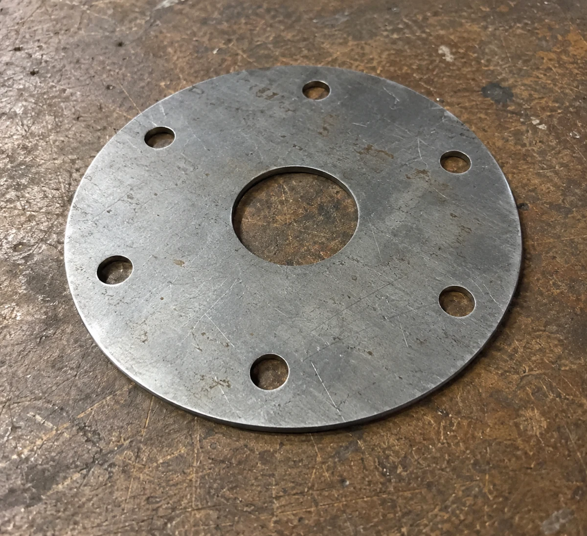 Synthetic photograph of a circular metal plate with six bolt holes and a central opening